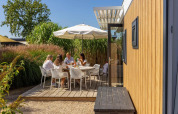 Gezin geniet van een maaltijd buiten bij Dune Lodge Family, Camping Zonneweelde, Nederland onder parasol.