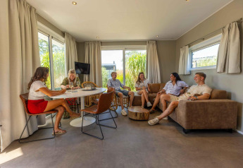 Gruppo di amici che si rilassa nella zona giorno di Dune Lodge Family al Camping Zonneweelde, Paesi Bassi.