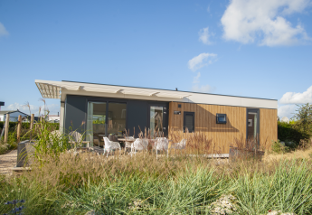 Moderne Dune Lodge Family op Camping Zonneweelde in Nederland, met gras en een terras met stoelen buiten.