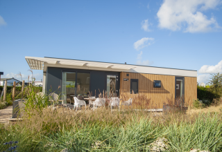 Moderne Dune Lodge Family ved Camping Zonneweelde i Holland, omgivet af græs og udendørs siddeplads.