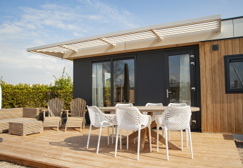 Buitenterras van Dune Lodge Family op Camping Zonneweelde, Nederland, met stoelen en tafel onder een zonneluifel.