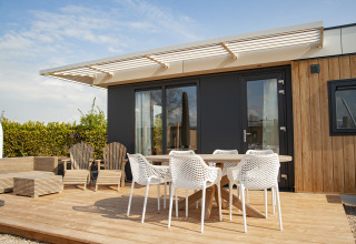 Terraza exterior en Dune Lodge Family en Camping Zonneweelde, Países Bajos, con sillas y mesa bajo toldo.