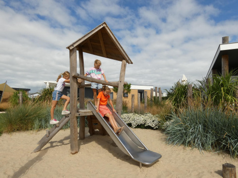 Børn leger på en legeplads med rutsjebane ved Dune Lodge Family på Camping Zonneweelde i Holland.