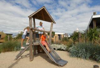 Børn leger på en legeplads med rutsjebane ved Dune Lodge Family på Camping Zonneweelde i Holland.