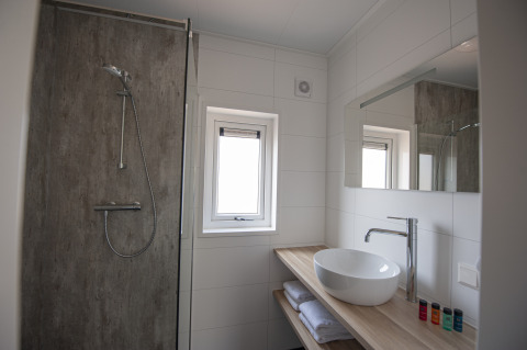 Baño moderno con ducha, lavabo, espejo y ventana en Dune Lodge Family, Camping Zonneweelde, Países Bajos.