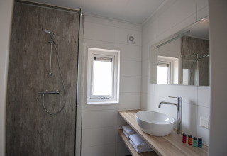 Baño moderno con ducha, lavabo, espejo y ventana en Dune Lodge Family, Camping Zonneweelde, Países Bajos.