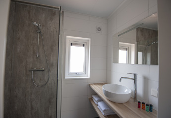 Moderne badeværelse med bruser, håndvask, spejl og vindue i Dune Lodge Family, Camping Zonneweelde, Holland.