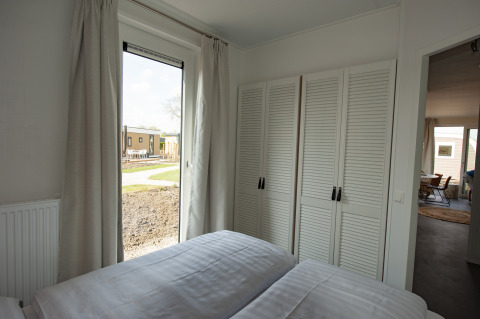 Slaapkamer in Dune Lodge Family op Camping Zonneweelde, Nederland, met kleerkast, raam en dubbel bed.