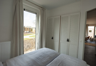 Slaapkamer in Dune Lodge Family op Camping Zonneweelde, Nederland, met kleerkast, raam en dubbel bed.