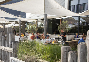 Outdoor dining area at Dune Lodge Family, Camping Zonneweelde, Netherlands, with people and staff.