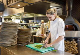 Una chef corta hierbas frescas en la cocina moderna de Dune Lodge Family en Camping Zonneweelde, Países Bajos.