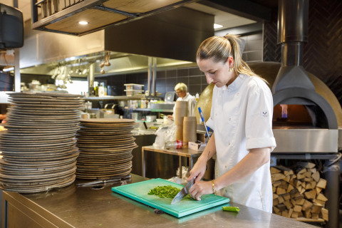 Una chef corta hierbas frescas en la cocina moderna de Dune Lodge Family en Camping Zonneweelde, Países Bajos.