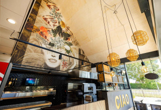 Interior view of Dune Lodge Family at Camping Zonneweelde with art mural, modern lights and large 'CIAO' sign.