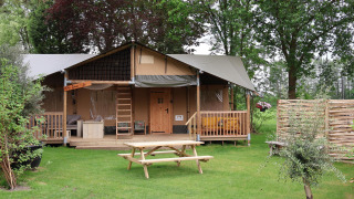 Tienda Safari Ranger DeLuxe con porche y mesas en césped del Camping Vossenberg en los Países Bajos.