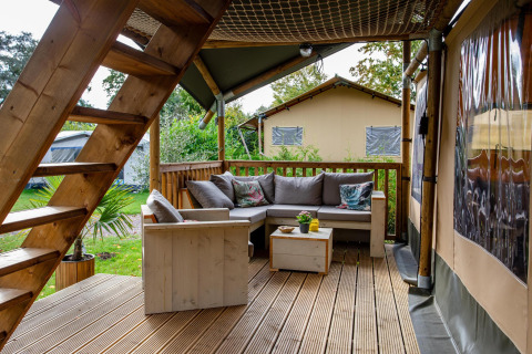 Terraza de madera con zona lounge en tienda Safari tent Ranger DeLuxe en Camping Vossenberg, Países Bajos.