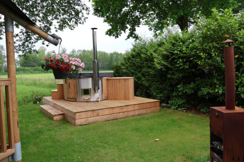 Zona exterior de una tienda safari con jacuzzi moderno, terraza de madera y vegetación en Camping Vossenberg.