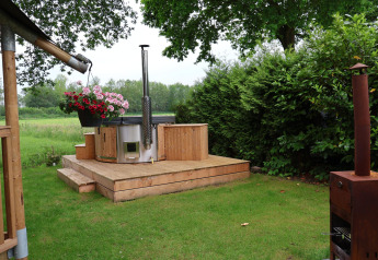 Outdoor setting with a modern hot tub, wooden deck, and greenery at Camping Vossenberg’s safari tent.