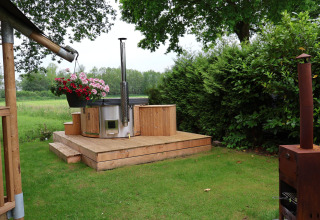 Zona exterior de una tienda safari con jacuzzi moderno, terraza de madera y vegetación en Camping Vossenberg.