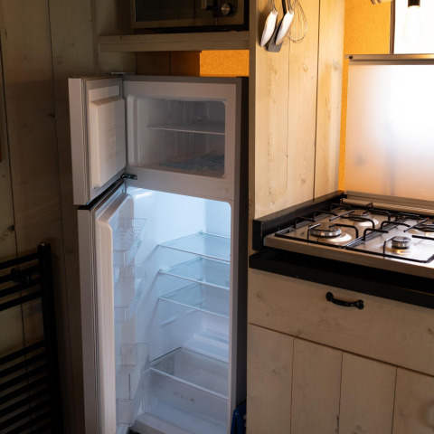 A kitchen with an open fridge and freezer inside Safari tent Ranger DeLuxe at Camping Vossenberg, Netherlands.