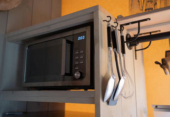 Microonde su mensola di legno con utensili da cucina appesi in una tenda safari al Camping Vossenberg, Paesi Bassi.