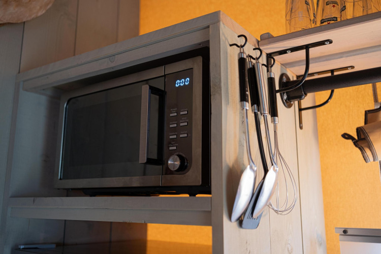 Microondas en un estante de madera con utensilios de cocina colgados en tienda safari de Camping Vossenberg.