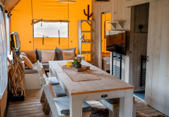 Vista interna della tenda Safari Ranger DeLuxe con tavolo da pranzo, divano e arredo in legno al Camping Vossenberg.