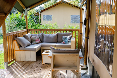 Acogedora zona de estar al aire libre con sofá y cojines en la terraza de una tienda safari en Camping Vossenberg.
