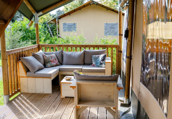 Gezellige zithoek met sofa en kussens op het houten terras van een safaritent bij Camping Vossenberg.