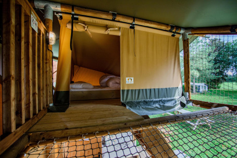 Vista interior de una tienda Safari Ranger DeLuxe con cama y red en Camping Vossenberg, Países Bajos.