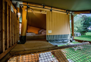 Vista interior de una tienda Safari Ranger DeLuxe con cama y red en Camping Vossenberg, Países Bajos.