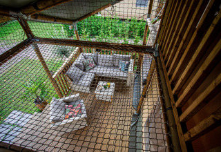 Vista superior de una terraza cubierta con muebles de jardín modernos y red de seguridad en Camping Vossenberg.