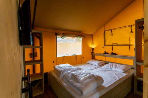 Vista interior de la tienda Safari Ranger DeLuxe con cama doble y luz cálida en Camping Vossenberg, Países Bajos.