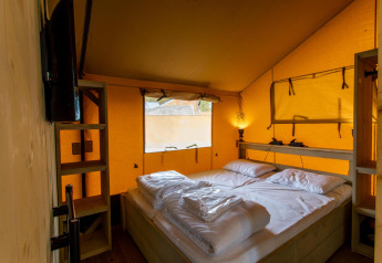 Vista interna della tenda Safari Ranger DeLuxe con letto matrimoniale e luce calda al Camping Vossenberg.