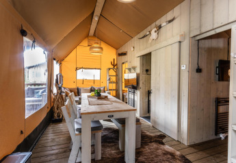 Vista interna della tenda Safari Ranger DeLuxe con tavolo da pranzo in legno e decorazioni rustiche.