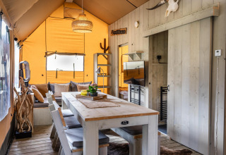 Interior de la tienda Safari Ranger DeLuxe con mesa de comedor, sofá y colores cálidos en Camping Vossenberg.