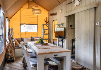 Interno della tenda Safari Ranger DeLuxe con tavolo da pranzo, divano e colori caldi al Camping Vossenberg.