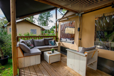 Zona de estar exterior en Safari tent Ranger DeLuxe con sofás y sillas en Camping Vossenberg, Países Bajos.