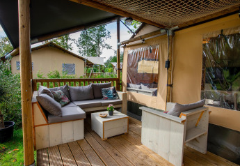 Area relax esterna della Safari tent Ranger DeLuxe con divano e sedie al Camping Vossenberg, Paesi Bassi.