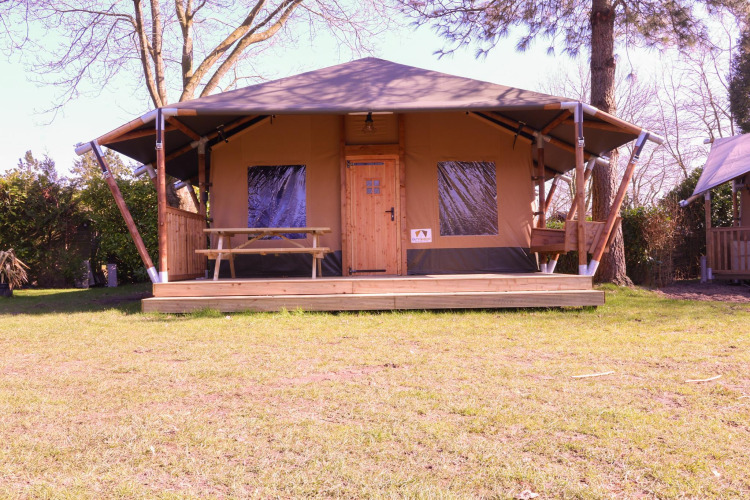 Tienda safari Cottage Kaa en Camping Vossenberg, Países Bajos, con terraza de madera y mesa de picnic.