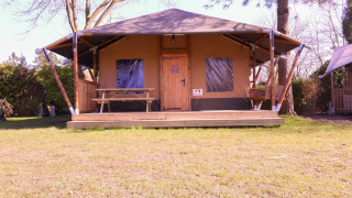 Safari-Zelt Cottage Kaa auf Camping Vossenberg in den Niederlanden mit Veranda und Picknickbank im Freien.