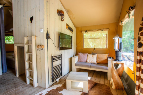 Interior de la tienda Safari Cottage Kaa en Camping Vossenberg, Países Bajos, con sofá y decoración natural.