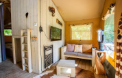 Interior de la tienda Safari Cottage Kaa en Camping Vossenberg, Países Bajos, con sofá y decoración natural.