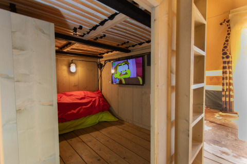 Habitación infantil en Safari tent Cottage Kaa con interior de madera, TV y decoración de jirafa en Camping Vossenberg.