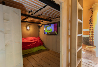 Habitación infantil en Safari tent Cottage Kaa con interior de madera, TV y decoración de jirafa en Camping Vossenberg.
