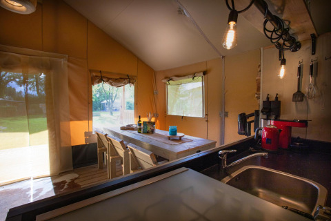 Interior de la tienda safari Cottage Kaa en Camping Vossenberg, Países Bajos, con mesa y cocina.