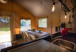Interior de la tienda safari Cottage Kaa en Camping Vossenberg, Países Bajos, con mesa y cocina.