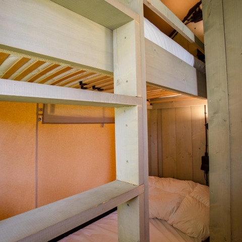 Literas de madera y luz acogedora dentro de la tienda Safari Cottage Kaa en Camping Vossenberg, Países Bajos.