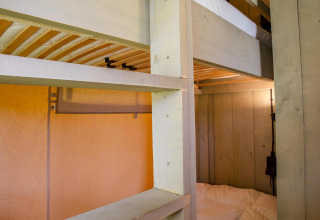 Literas de madera y luz acogedora dentro de la tienda Safari Cottage Kaa en Camping Vossenberg, Países Bajos.
