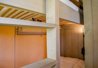 Wooden bunk beds and cozy lighting inside Safari tent Cottage Kaa at Camping Vossenberg in the Netherlands.
