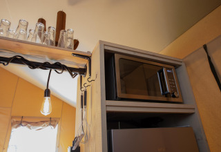 Zona de cocina en Safari tent Cottage Kaa con microondas, estante de vasos y batidor colgante en Holanda.